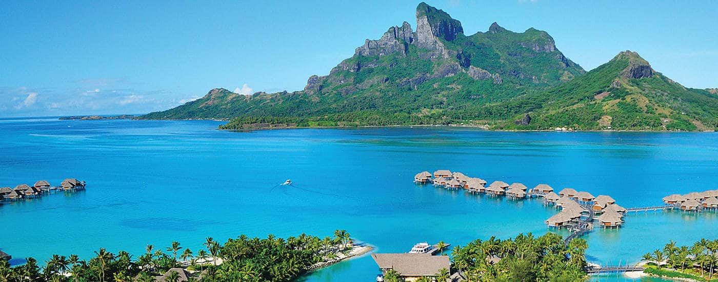 Overwater bungalows in blue sea with green tropical mountain behind
