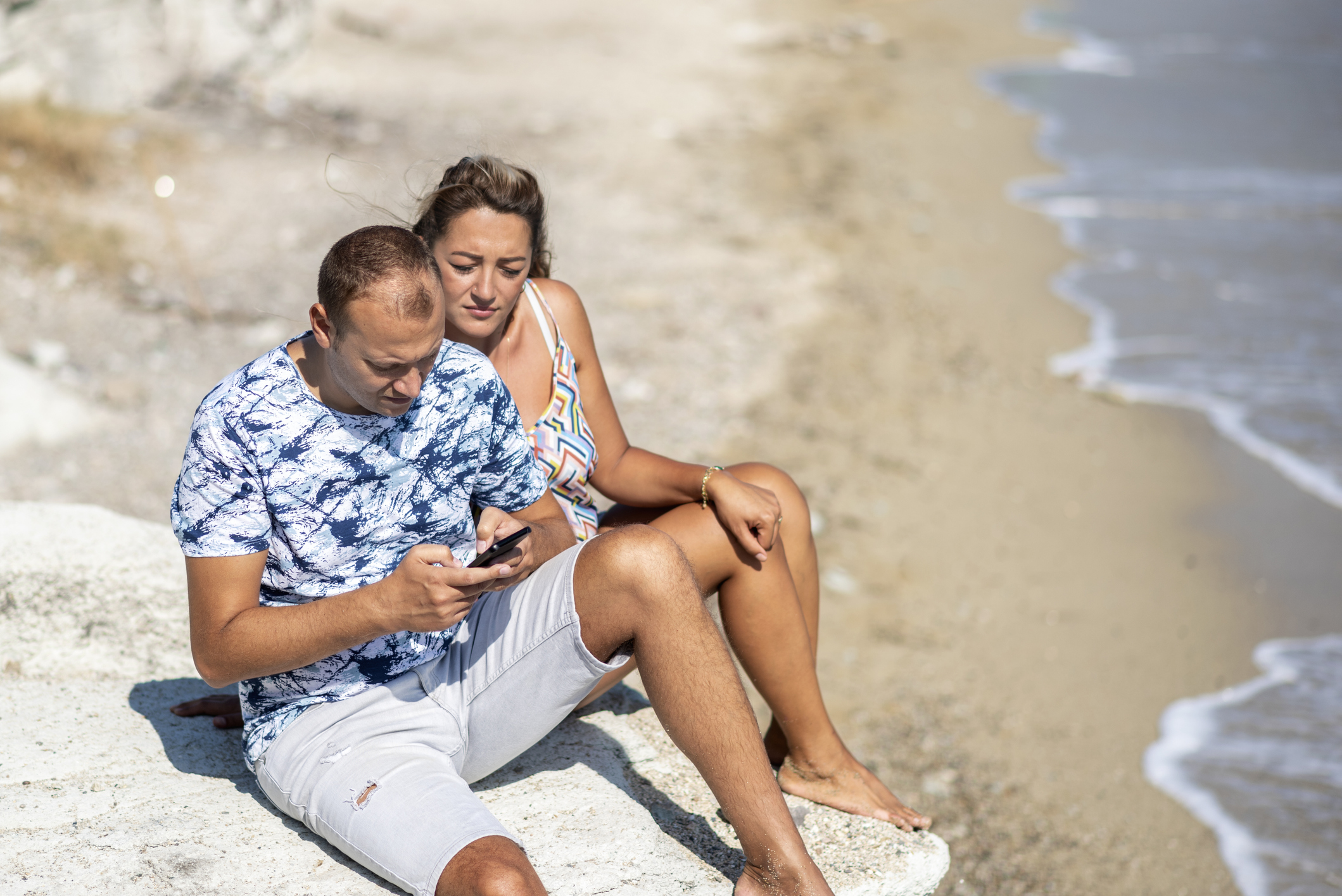 couple checking their phone by the shore